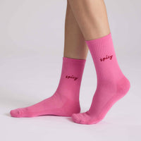 Pink socks with 'spicy' text worn by a person on a light gray background